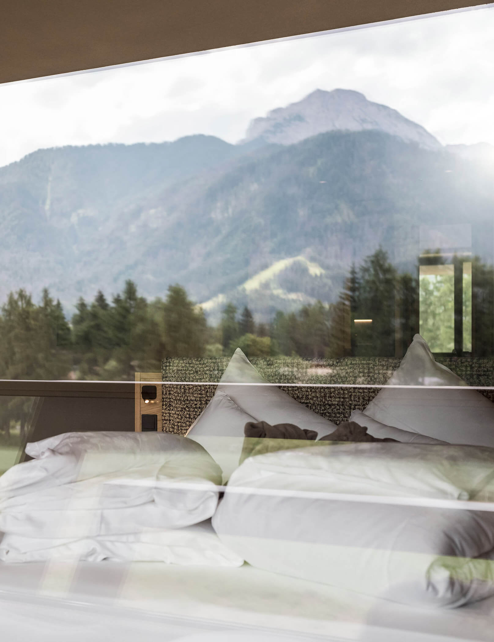 Letto matrimoniale con coperte bianche, alberi e montagne di Dobbiaco riflessi nel vetro della finestra - Hotel Patris
