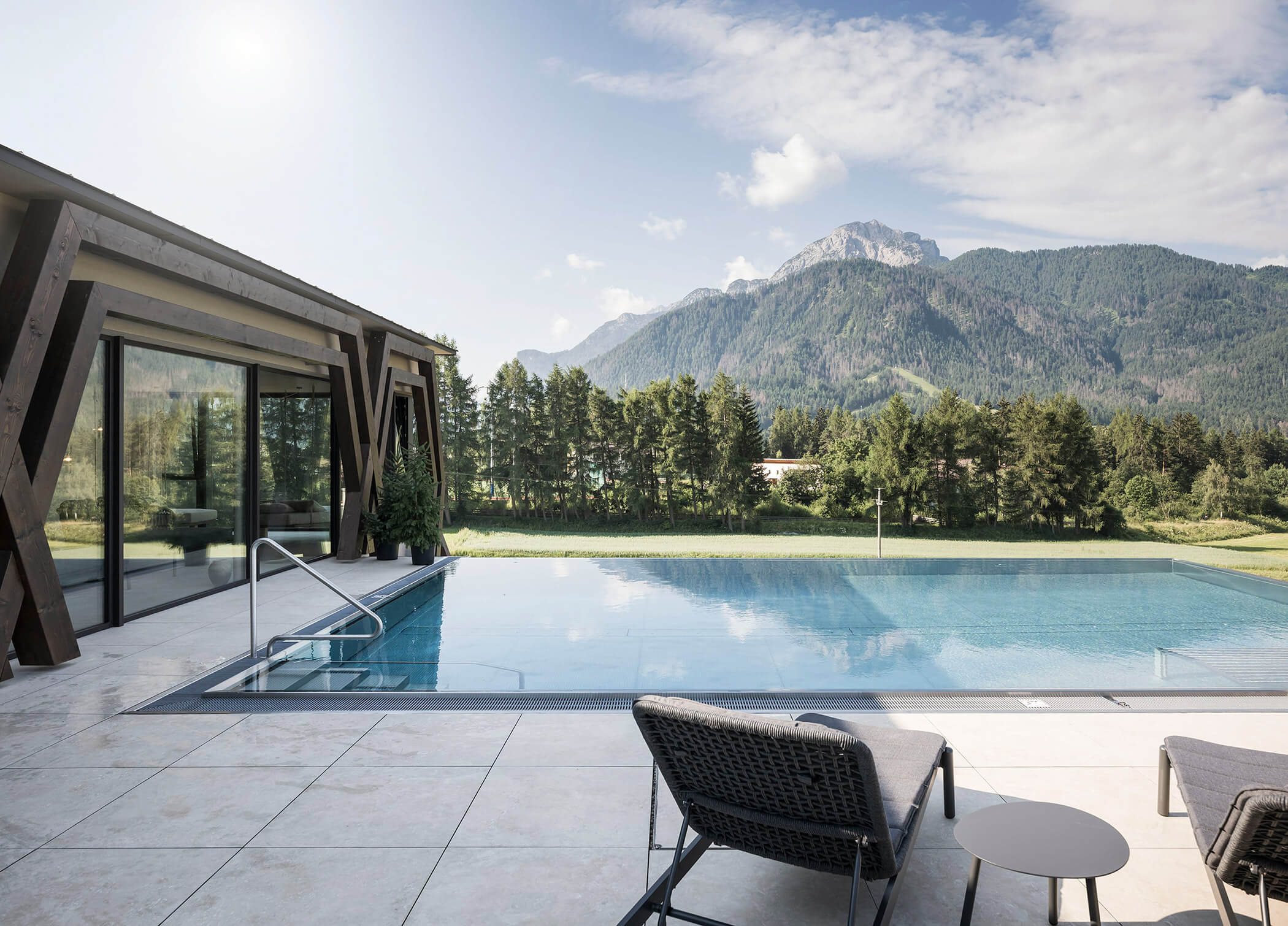Außenpool mit zwei Sonnenliegen, im Hintergrund Bäume und Berge - Hotel Patris