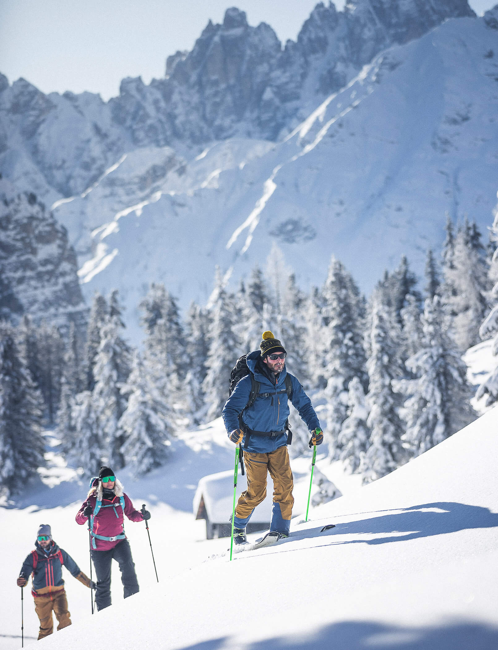 Drei Skitourengeher im Neuschnee, im Hintergrund eine verschneite Hütte, Bäume und Berge - Hotel Patris