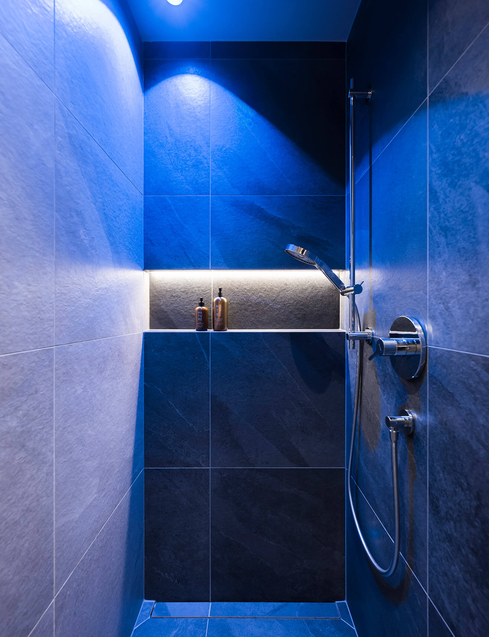 Doccia con piastrelle in pietra e illuminazione blu - Hotel Patris