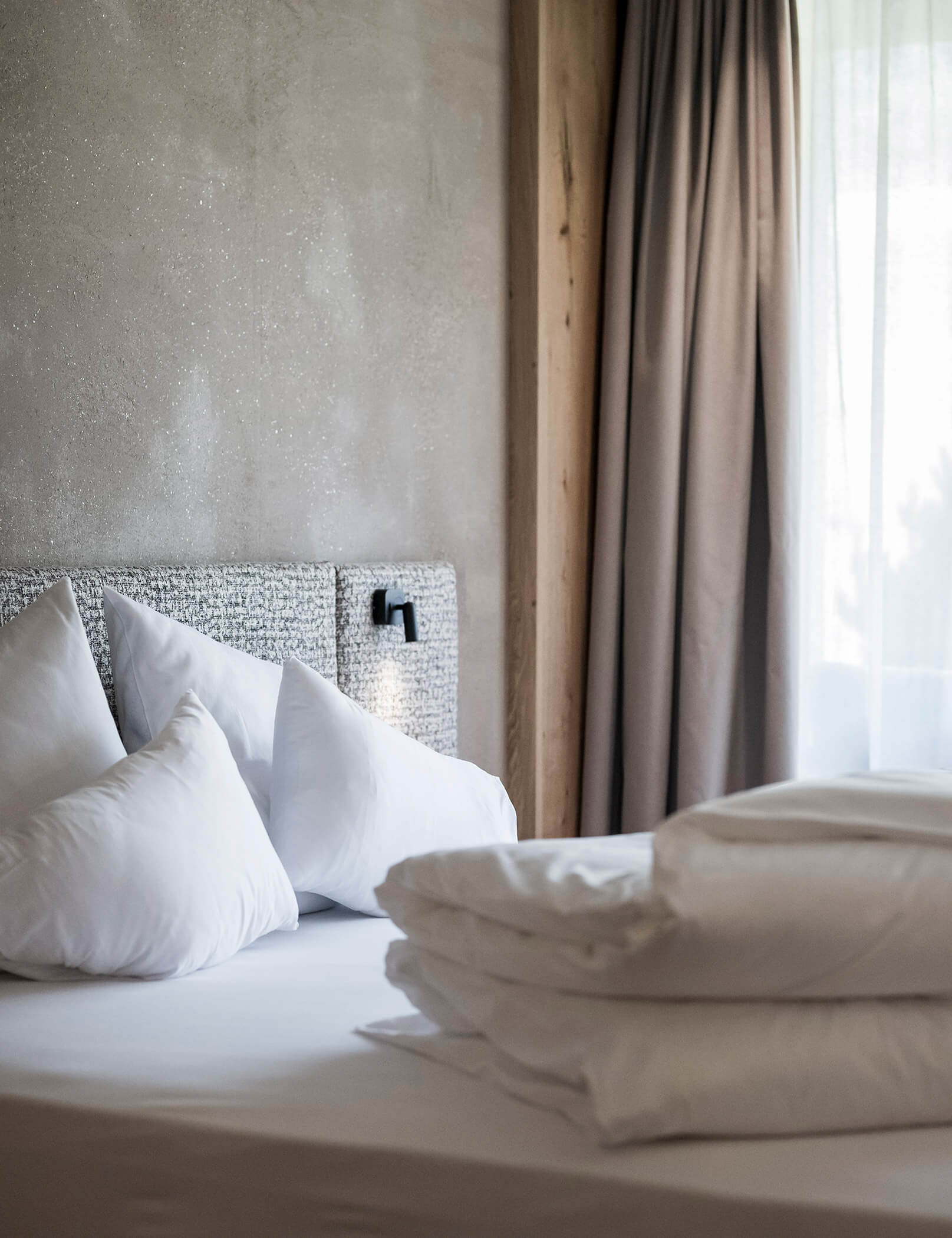 Bett mit weißer Bettwäsche und grauer Wand - Hotel Patris